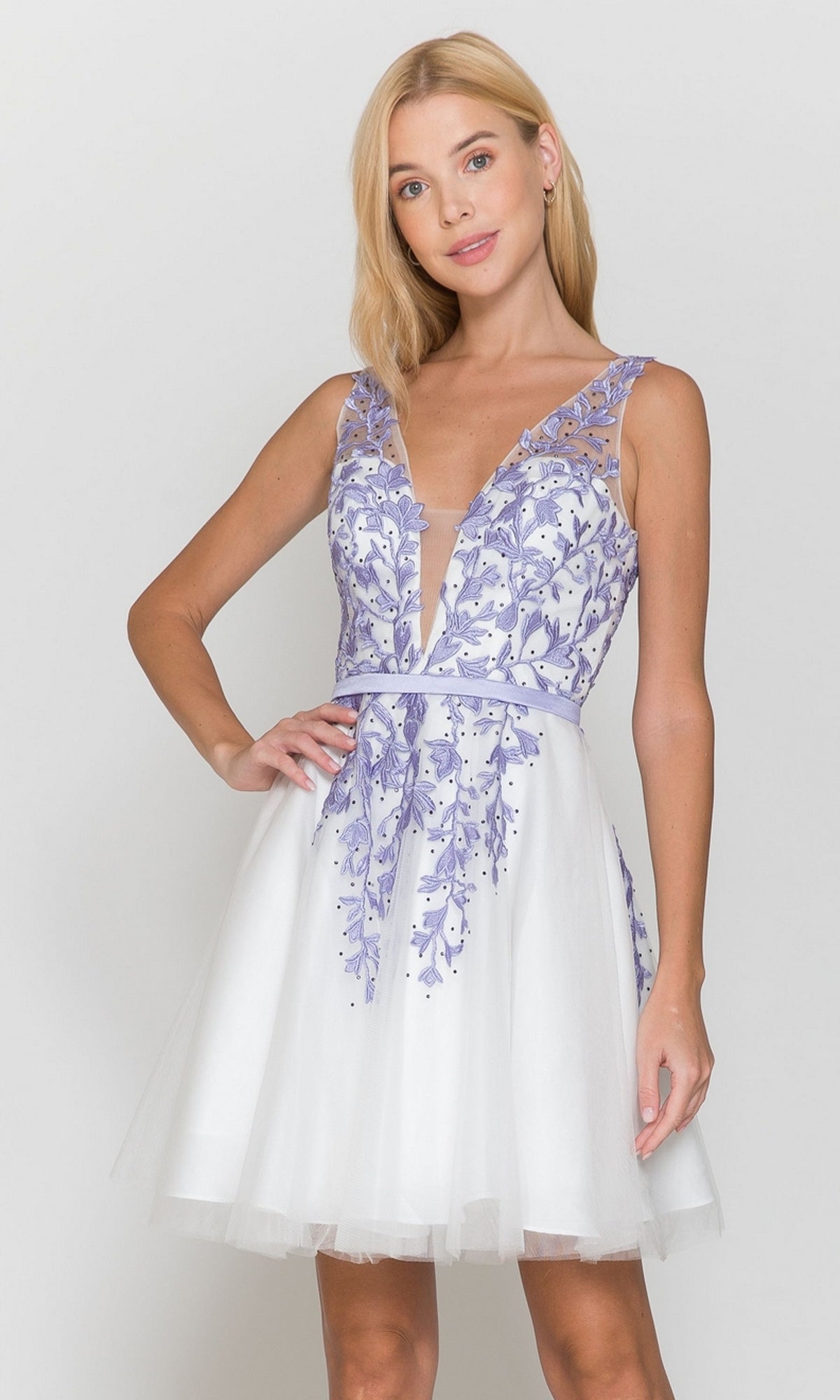 A woman wears the Tulle and Lace Short A-Line Homecoming Dress 8696 in white/lilac, featuring a sleeveless semi-formal design, standing against a plain background.